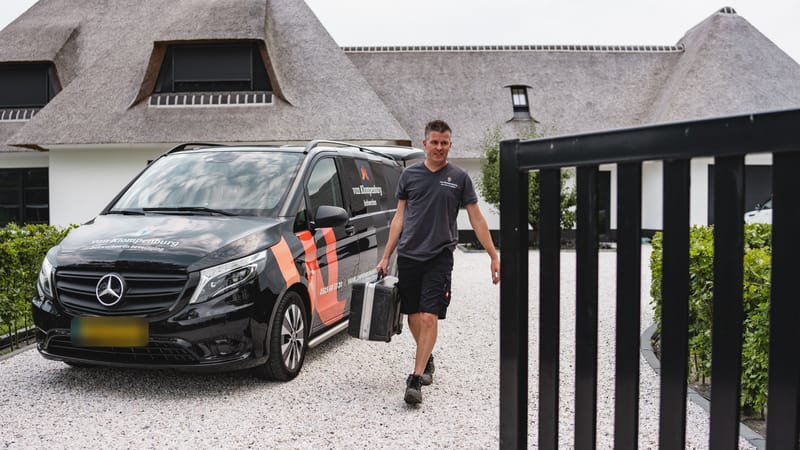 Monteur loopt met een koffer van de bedrijfsbus naar een poort