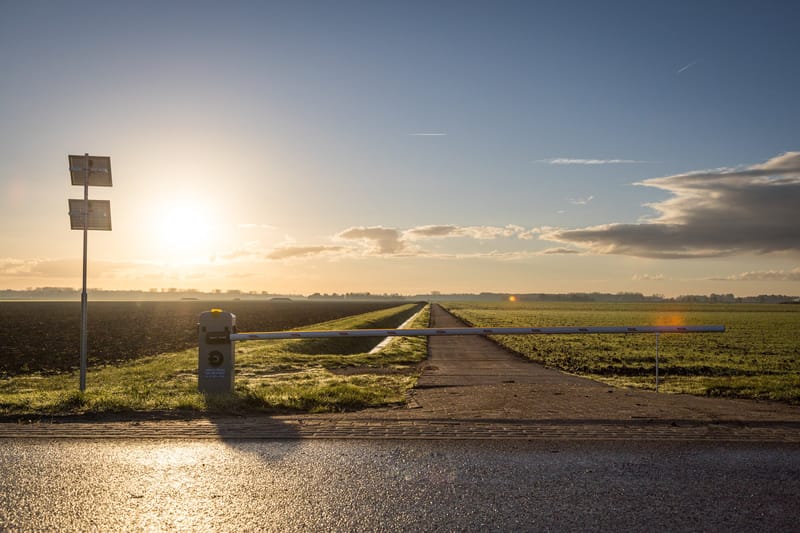 Slagboom op zonne-energie over een landweg, met de zon laag boven de polder