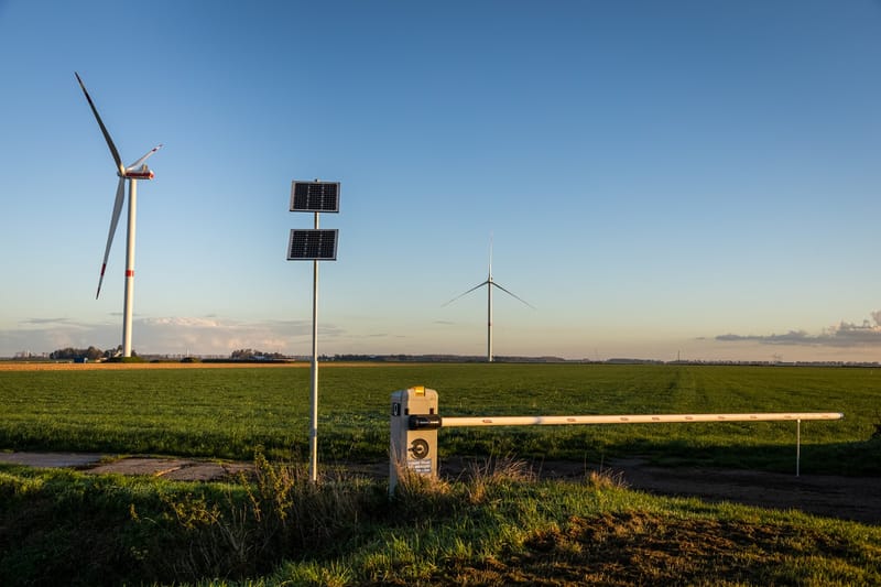 Slagboom met zonnepanelen op een mast langs een landweg bij Dronten, met windmolens op de achtergrond