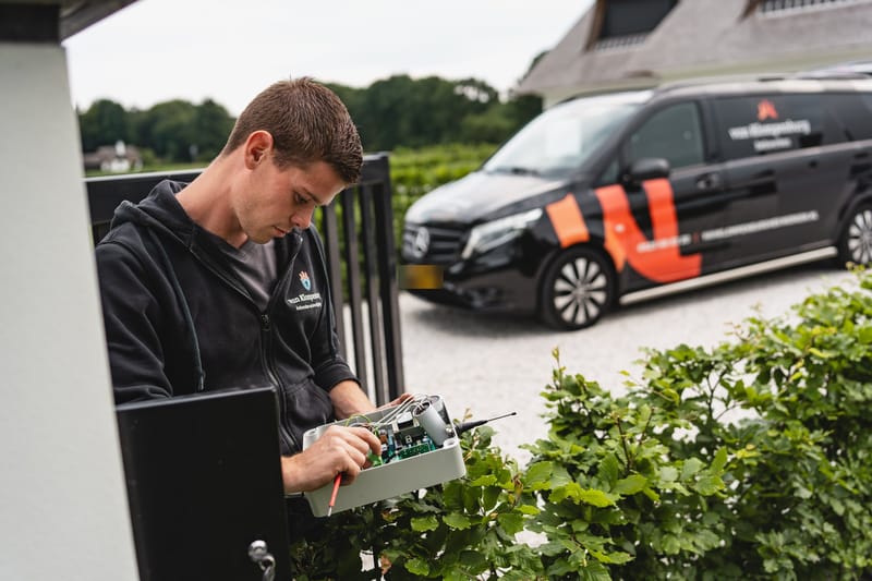 Monteur werkt aan de besturing van een poort, met de bedrijfsbus op de achtergrond