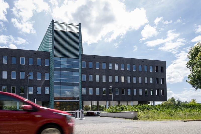 Auto rijdt langs een kantorencomplex met slagbomen bij de inrit