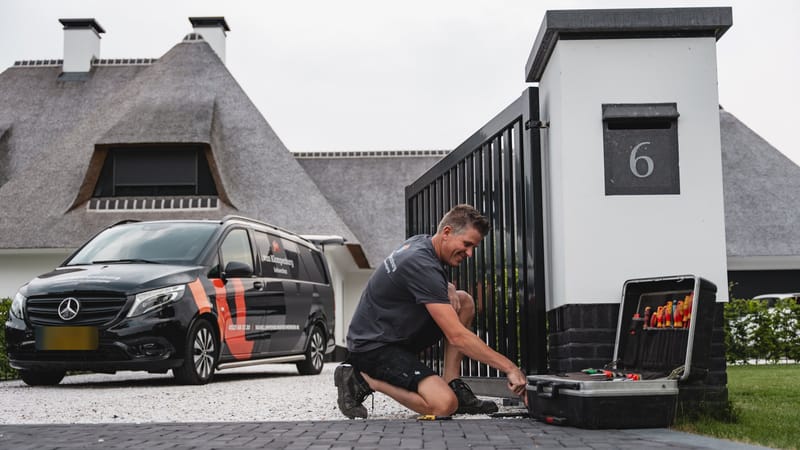 Monteur met gereedschapskoffer bij een poort, met de bedrijfsbus van Van Klompenburg