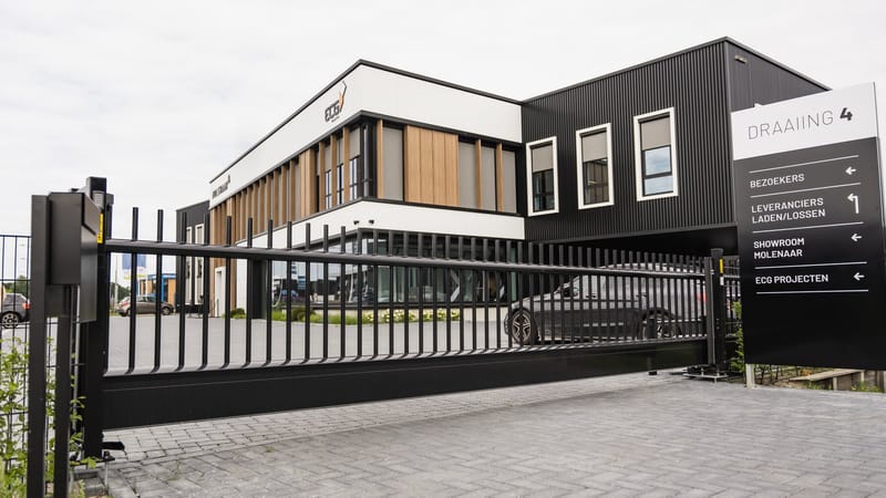Schuifpoort bij de inrit van een bedrijfspand, met bewegwijzering voor leveranciers