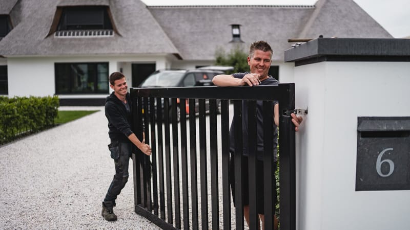 Twee monteurs van Van Klompenburg plaatsen een poort bij een woning